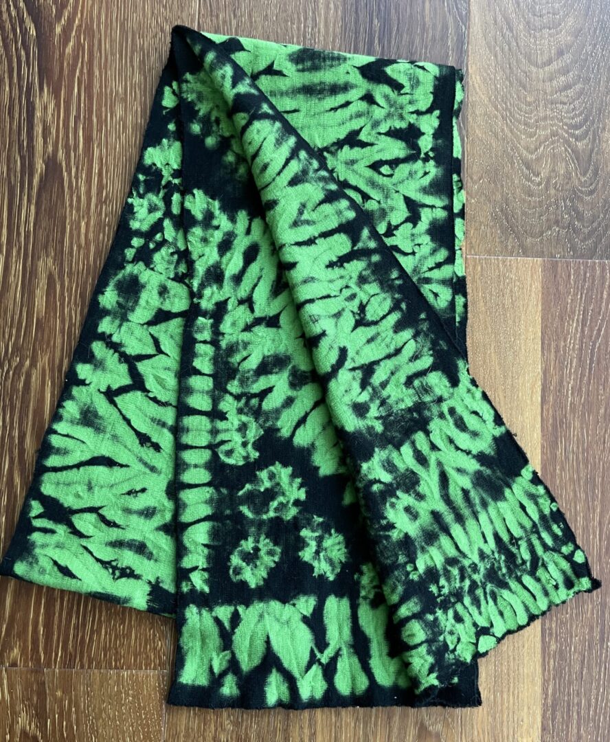 A green and black tie dye scarf on the floor